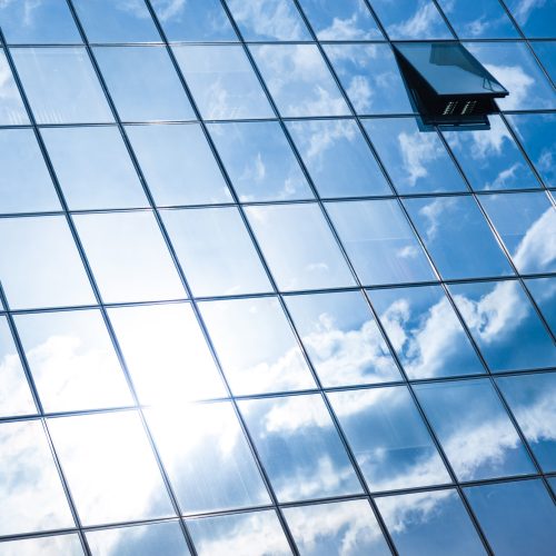 Modern facade of glass and steel. Modern facade of glass and steel with open window reflecting sky and clouds.